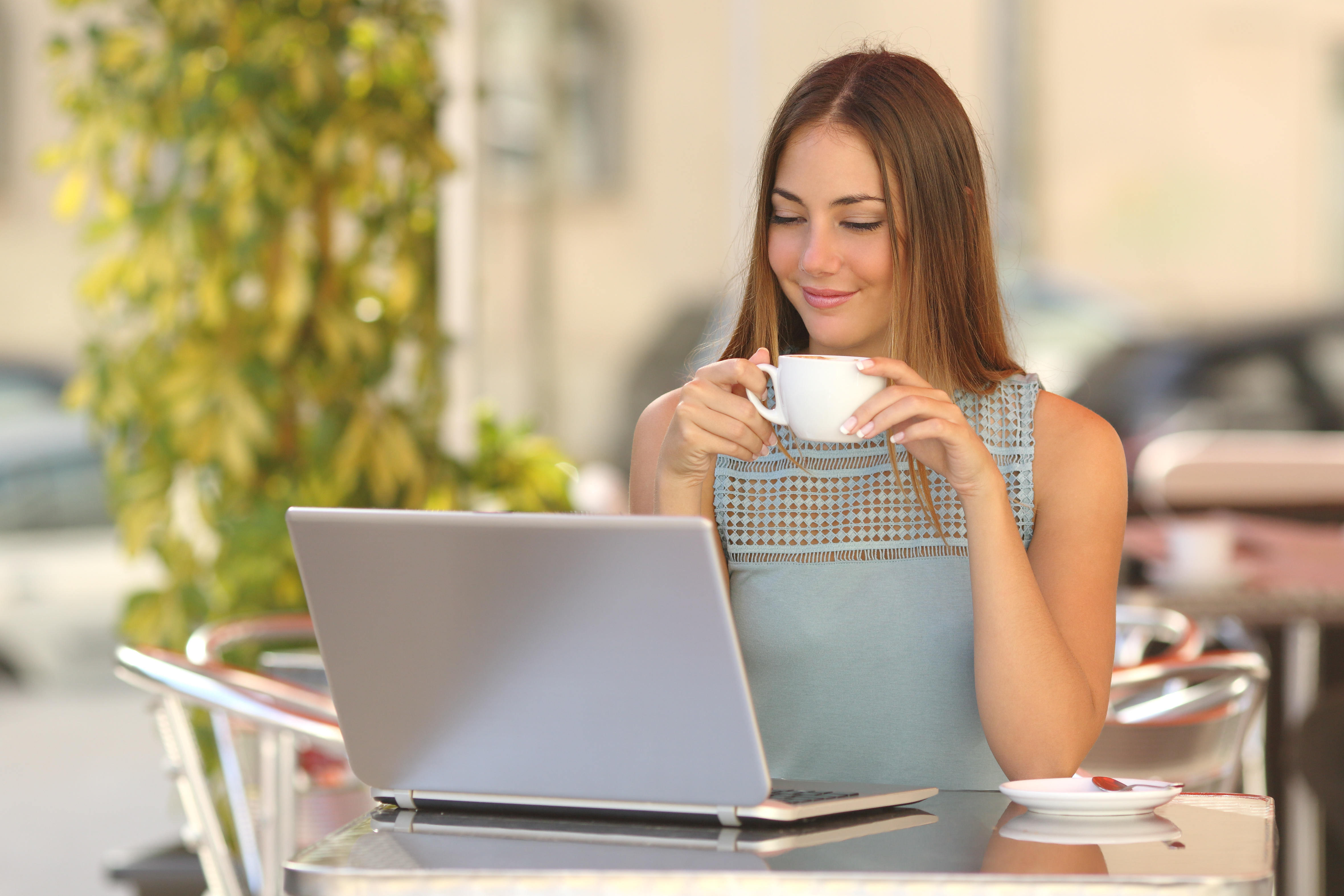 Relaxed woman watching laptop and holding a cup of coffee