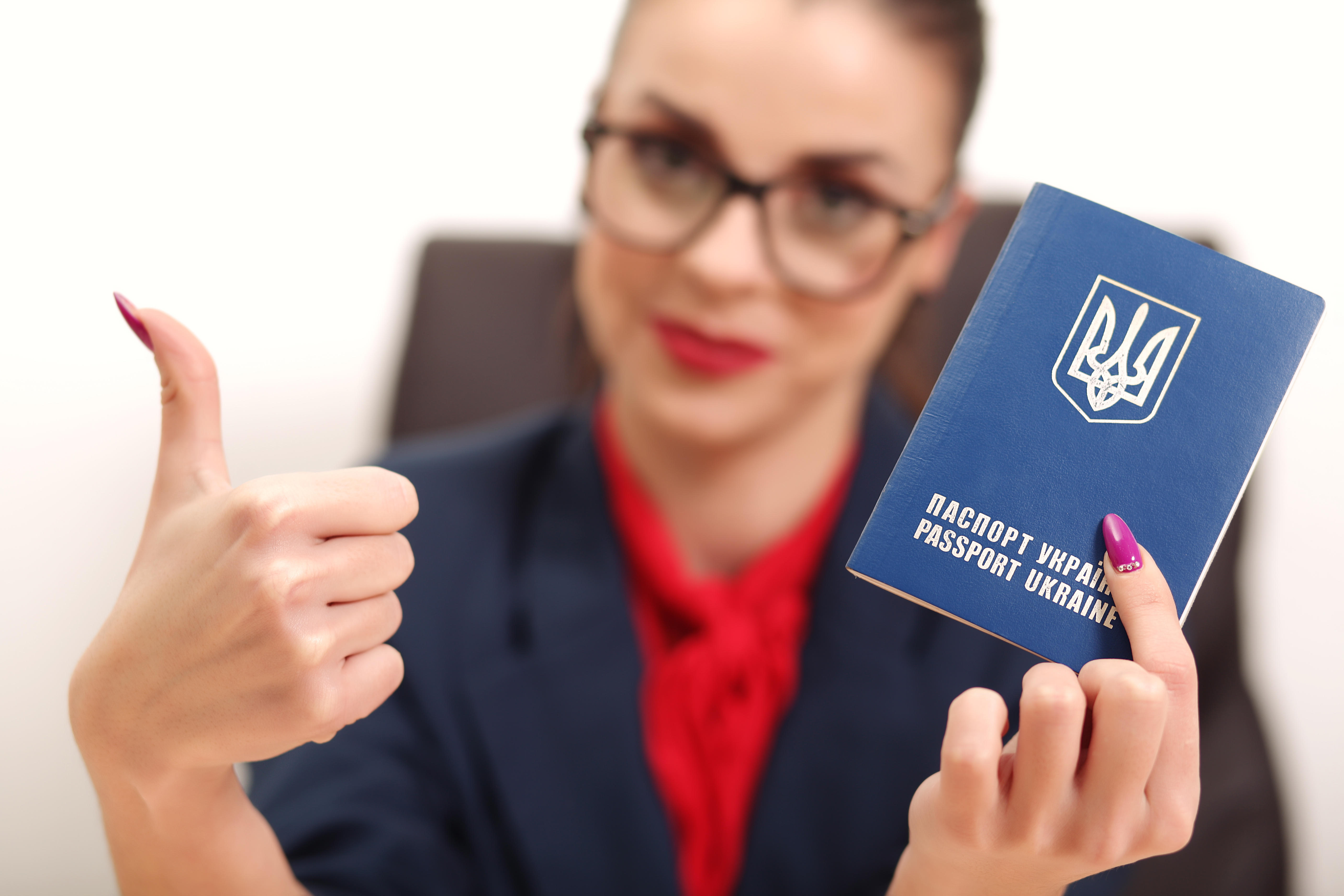 Beautiful young woman holding a passport Ukraine and raised thumb up
